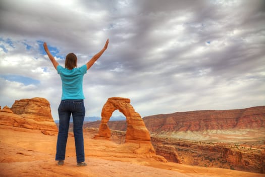 Woman with raised hands staying in front of Delicate Arch, Utah