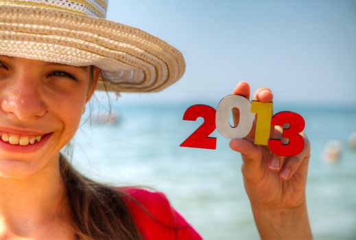 Teen girl at a beach holding wooden number '2013'