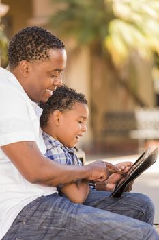 Happy African American Father and Mixed Race Son Having Fun Using Touch Pad Computer Tablet Outside.