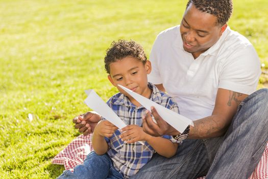 Happy Mixed Race Father and Son Playing with Paper Airplanes in the Park.
