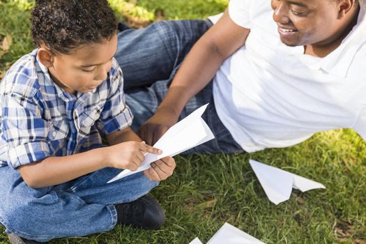 Happy Mixed Race Father and Son Playing with Paper Airplanes in the Park.
