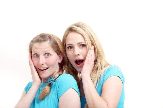 Two wide eyed female friends reacting in astonishment and incredulity as they stand close together with their hands to their cheeks