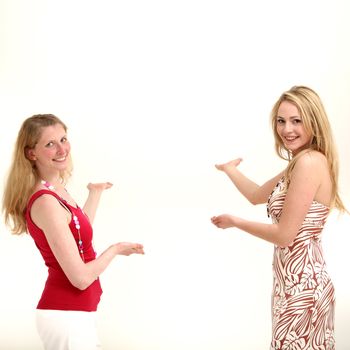 Two attractive friendly women standing facing each other with their palms out and other hands pointing to copyspace behind them as they coordinate a product placement concept