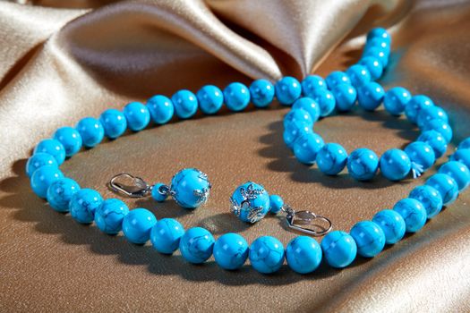 Blue necklace and earrings on a brown fabric