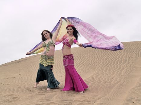 Posing of two arab dancers at desert holding some color clothes