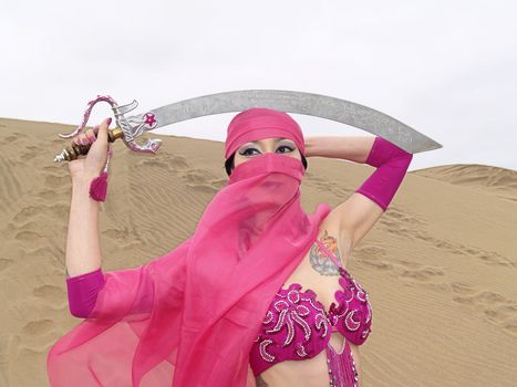 Portrait of a young veiled woman at desert with a sabre over her head