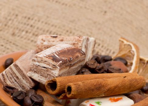 Sweets, cinnamon, nuts and coffee beans on a saucer, on burlap background.