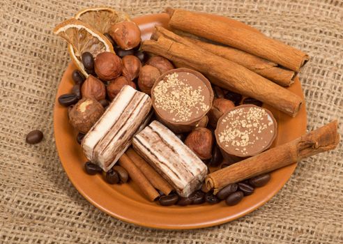 Sweets, cinnamon, nuts and coffee beans on a saucer, on burlap background.