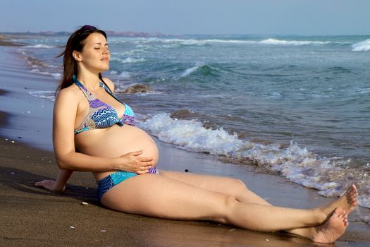 Gorgeous female model with big belly getting sun on the beach