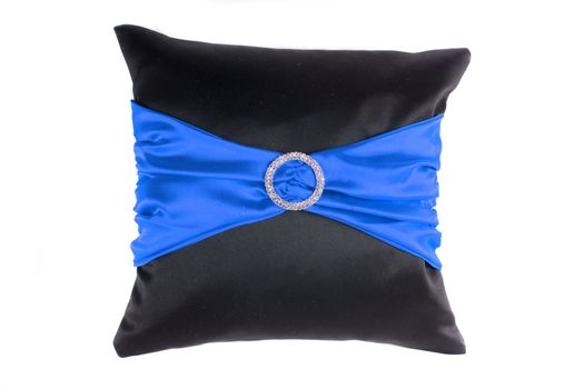 A designer pillow with blue satin and a brooch studded with jewels, on white studio background.