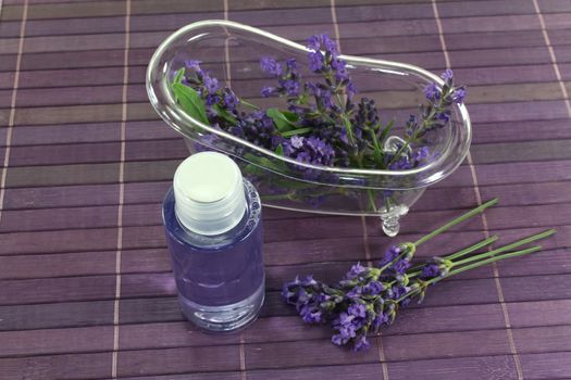 Lavender oil before a bath with flowers and leaves on violet background