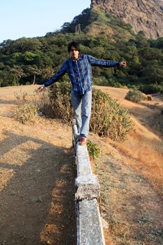 A young Indian man trying to balance himself while walking on a cement beam.