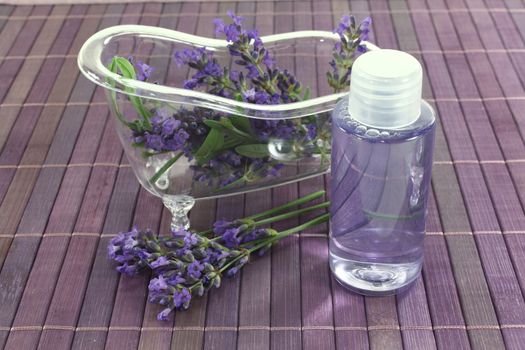 Lavender oil before a bath with flowers and leaves on purple background