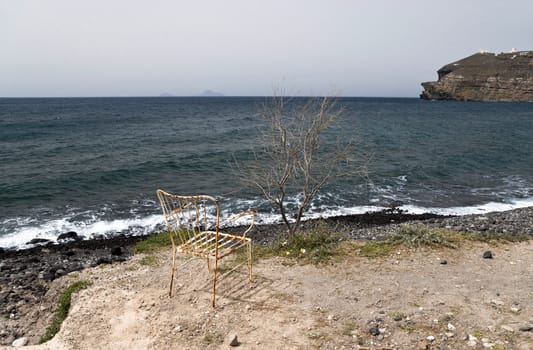 Lonely rusty chair and dry tree next to the sea