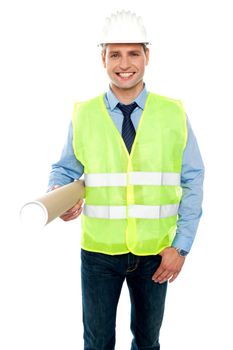 Smiling young architect holding blueprints wearing helmet and safety jacket
