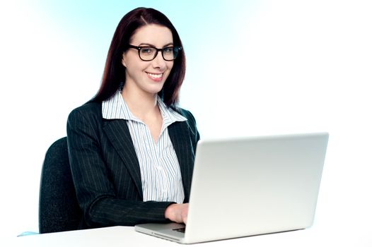 Cheerful corporate woman using laptop sitting in office