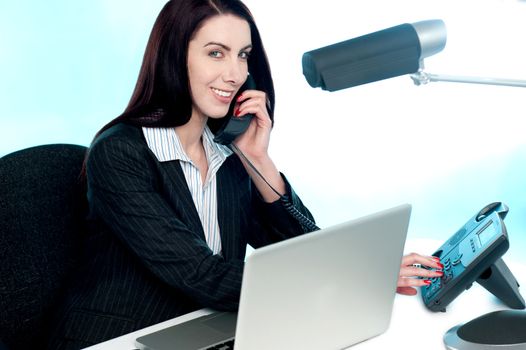 Secretary at work in office talking to client via phone call. Smiling and looking at camera