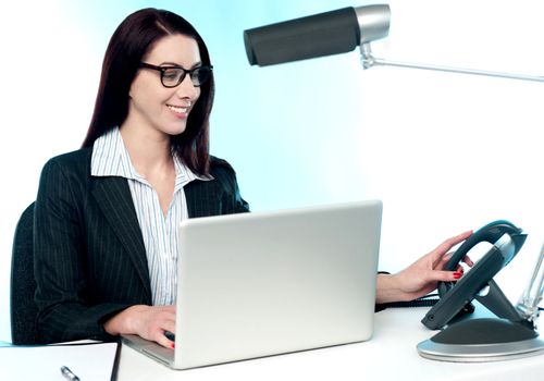 Female secretary answering phone call in office. Working on laptop