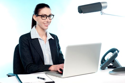 Smiling female secretary working on laptop. Indoor office shot