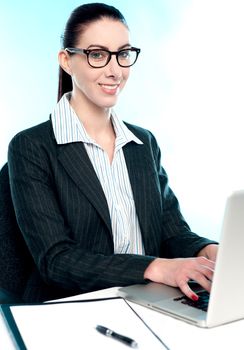 Corporate woman typing on laptop while looking at camera