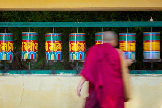 Buddhist monk passing and rotating prayer wheels on kora around Tsuglagkhang complex in McLeod Ganj, Himachal Pradesh, India