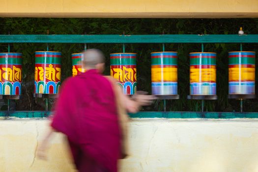 Buddhist monk passing and rotating prayer wheels on kora around Tsuglagkhang complex in McLeod Ganj, Himachal Pradesh, India