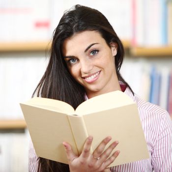 smiling female student with book in hands in a bookstore - model looking at camera. 