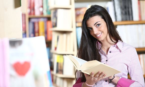 smiling female student with book in hands in a bookstore - model looking at camera. 