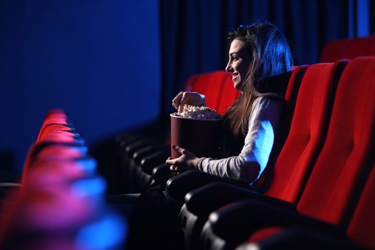 funny movie: portrait of a pretty young woman, eats popcorn and smiles, side view