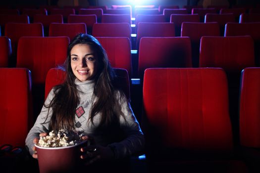 a pretty girl alone sitting in a empty movie theater, she eats popcorn and smiles