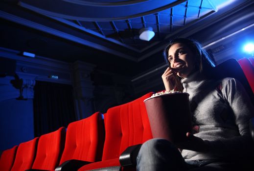 a pretty young woman sitting in an empty theater, she eats popcorn and smiles