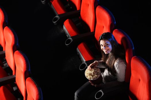 a pretty young woman sitting in an empty theater, eats popcorn and smiles, top view