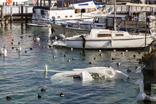 Boats in harbour, with one damaged by winter sinking in water.