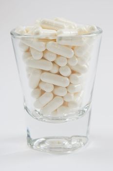 close up white pills  in glass  on white 