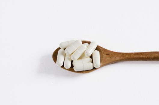 white pills on wooden spoon,   on white background