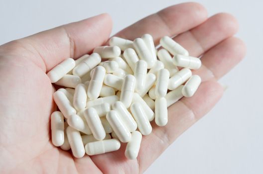 many white  pills spilling on hand with white background