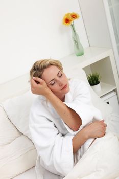 Beautiful woman dreaming as she slowly awakens while sitting in her bed in a white towelling gown