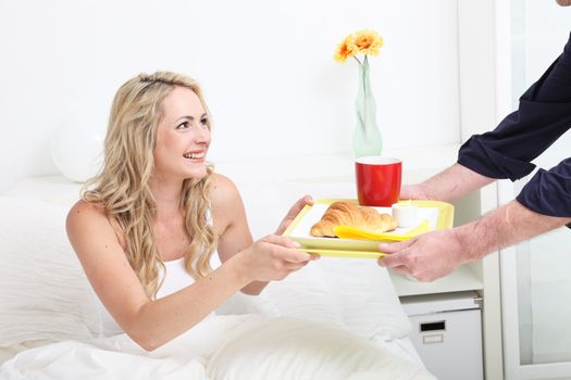 Beautiful blonde woman being treated to breakfast of croissant and coffee in bed