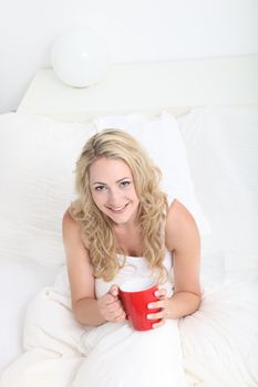 High angleview of a young woman drinking coffee in a large white bed