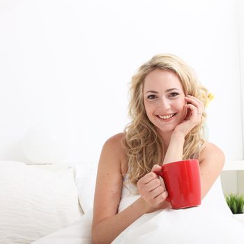 Radiant smiling woman sitting in bed with a large mug of early morning coffee