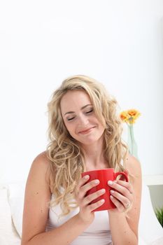 Beautiful woman enjoying the aroma of a hot mug of coffee as she relaxes in bed in the morning