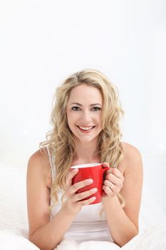 Smiling happy young woman looking refreshed after a good nights sleep enjoying a mug of coffee in bed