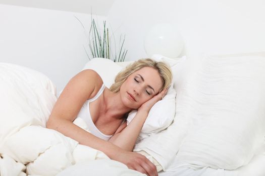 Natural pose of an attractive young lady sleeping peacefully in bed surrounded by white bedclothes