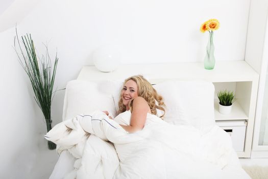 High angle view of a beautiful woman with long wavy blonde hair snuggling down in a white bed