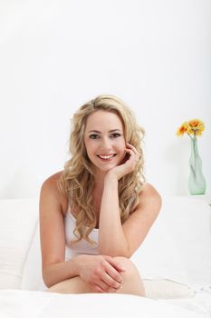 Gorgeous young blonde woman relaxing on her bed with her chin resting on her hand and a lovely radiant smile