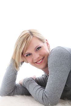 Woman relaxing on a carpet with her head leaning on her elbow and a lovely bright friendly smile