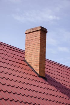 Brown tiled roof and yellow brick chimney on background of cloudy sky.