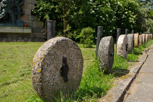 Retro rock millstones hanging on metal columns. Car parking decorations in park.