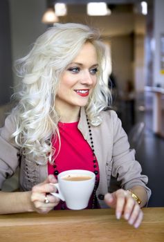 happy blonde in cafe at little table with cup of coffee
