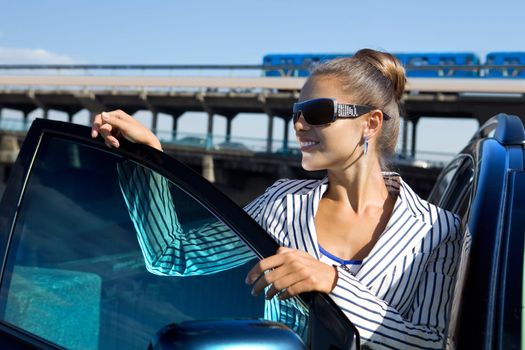 business woman in sunglasses near the car against city bridge